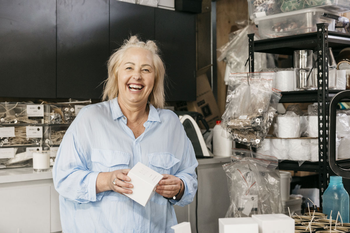A woman is in a workshop holding a small cardboard box, she's laughing