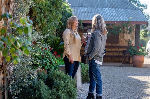 Photo of two women standing in the garden of a winery, holding wine glasses