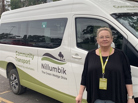 A woman stands in front of a white van, looking at the camera.