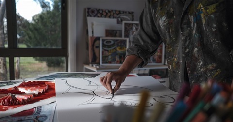 Photo of an artist in their studio, drawing on a large piece of paper with charcoal
