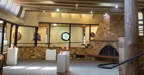 Photo of the interior of the Eltham Library Community Gallery. The walls are brown brick and there are several small sculptures on plinths 