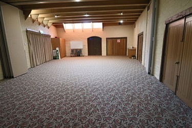 Large empty room with patterned carpet and timber ceiling beams