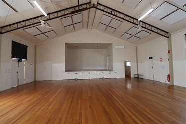 A large room with peaked ceiling and timber floorboards and a raised platform at the end of the room
