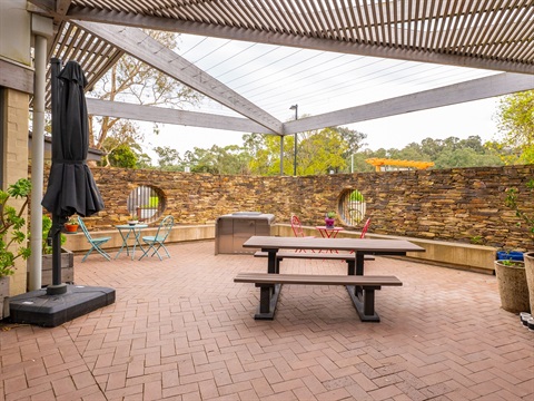 A paved space is covered by large beams and shade cloth