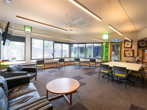 A wide open indoor space surrounded by windows and featuring tables and chairs around the edge of the room