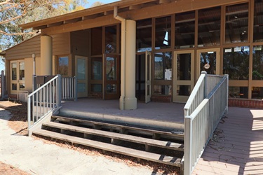 A shaded veranda in front of a building and three wide steps down to the path