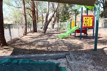 An enclosed playground with colourful equipment and lots of tree coverage