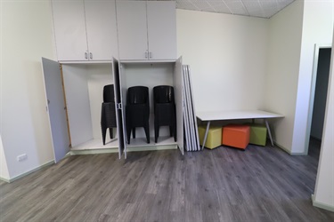 A light room with cupboards open revealing stacked chairs, and a table in the corner with cube seats underneath