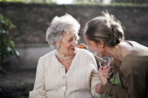 Older woman in beige cardigan talking closely with another woman in green shirt