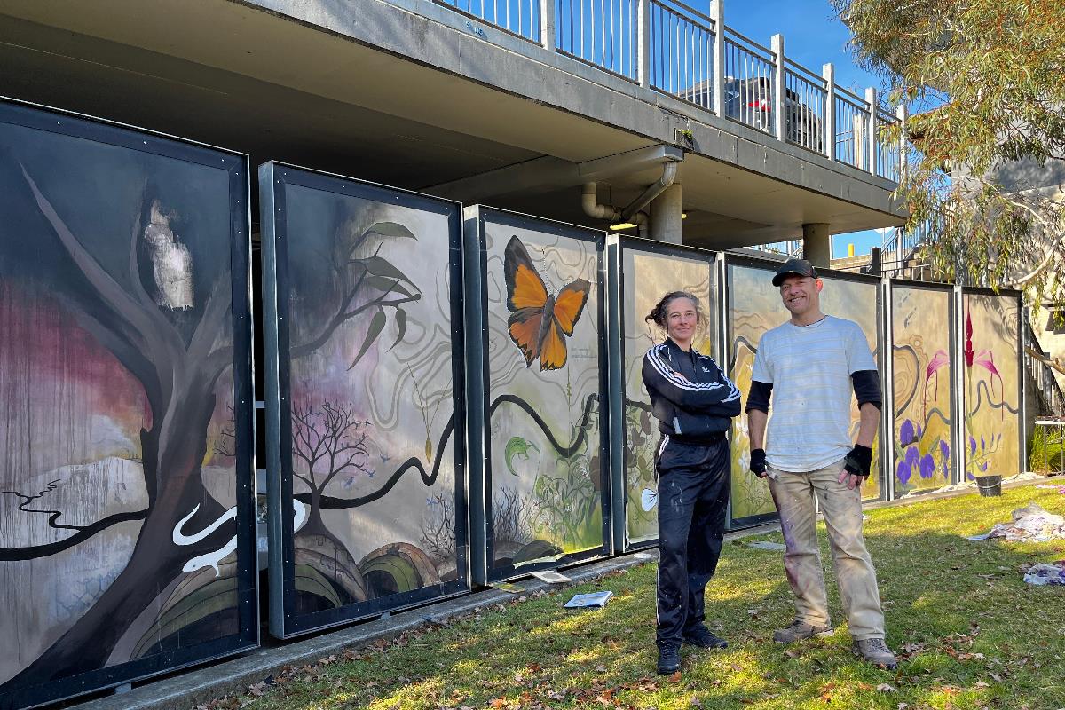 Two artists stand proudly in front of a large mural