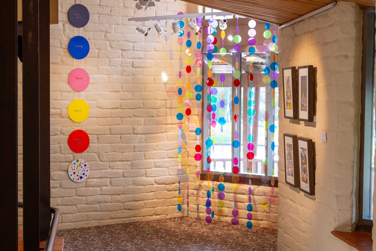 Photo of coloured circles installed in front of a window at the gallery with four photographic works hanging on the right hand side