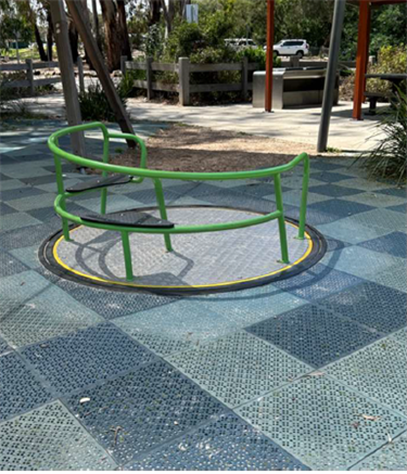 Circular concrete base is surrounded by a bright green handrail and a soft floor in a playground