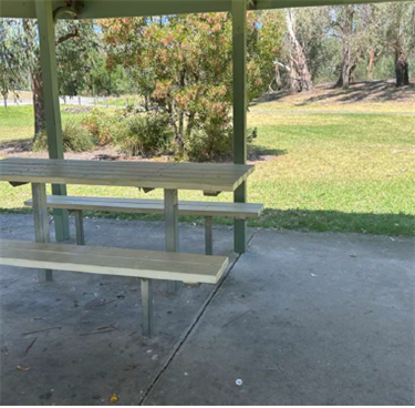 A table with two bench seats on either side on concrete under a shelter