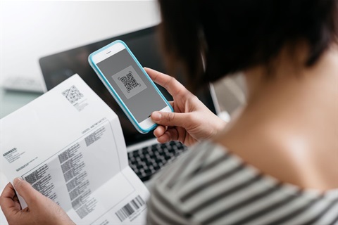 This is a photograph of a woman scanning the QR code on a bill with her mobile phone.