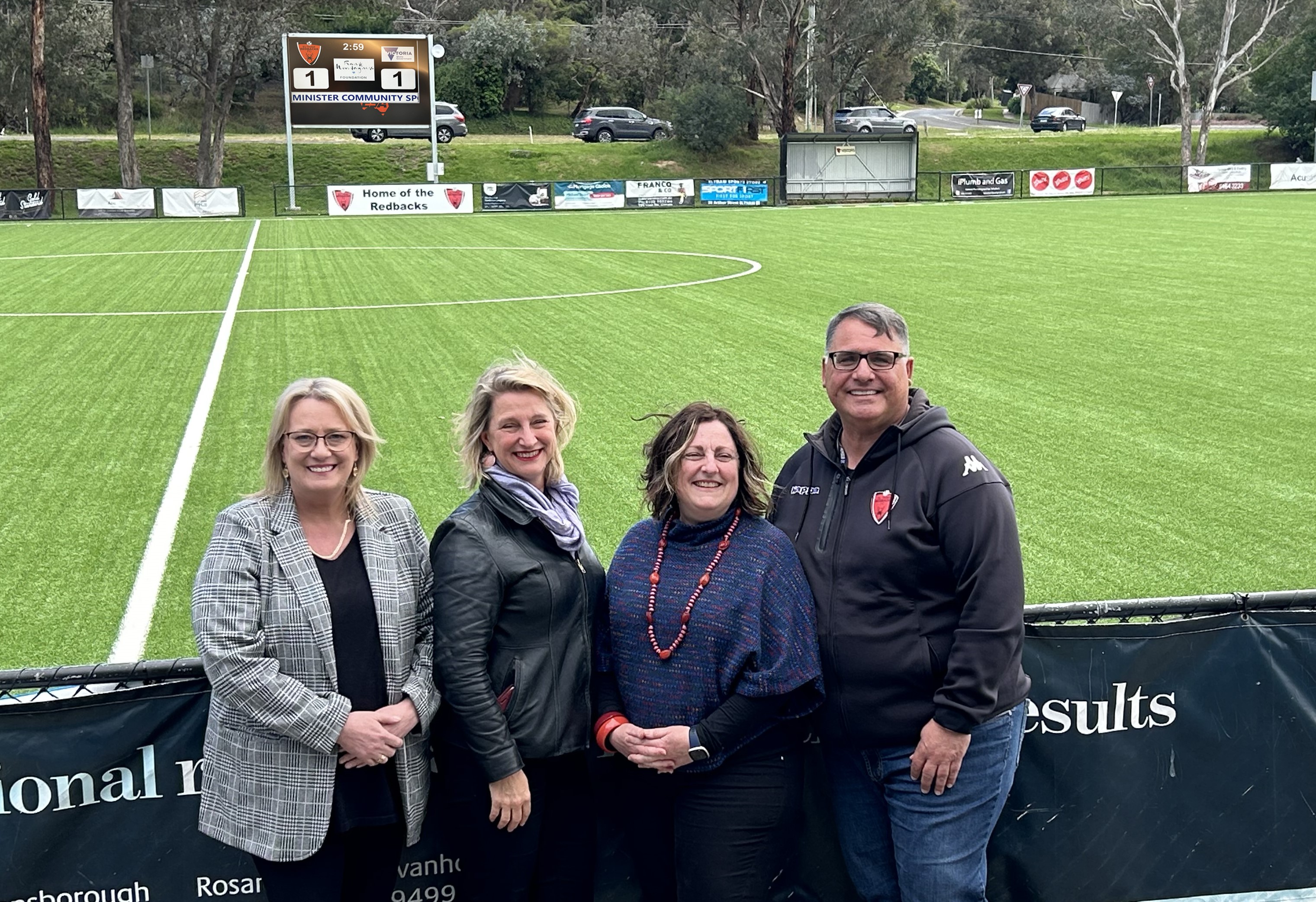 This is a photograph of Community Sport Minister Ros Spence, Eltham MP Vicki Ward, Cr Frances Eyre and Eltham Redbacks Chairman Ivan Della Costa at the Redbacks ground in Eltham North with the new scoreboard in the background.