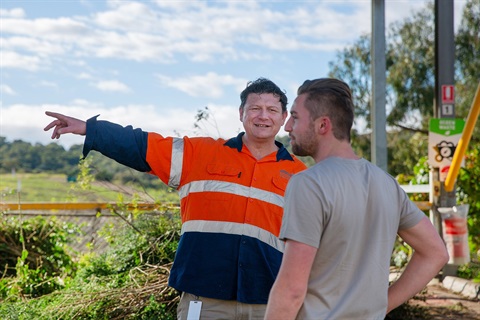 Photo of two men having a conversation. One man is wearing high-vis clothing and is pointing into the distance.