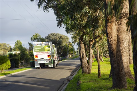 Photo of a suburban street. There is a Nillumbik rubbish collection truck driving away down the street.