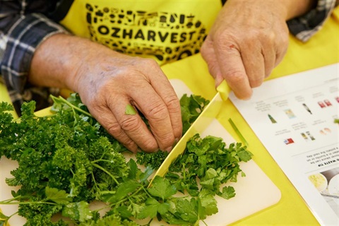 Close up of hands chopping fresh herbs on a bright yellow chopping board