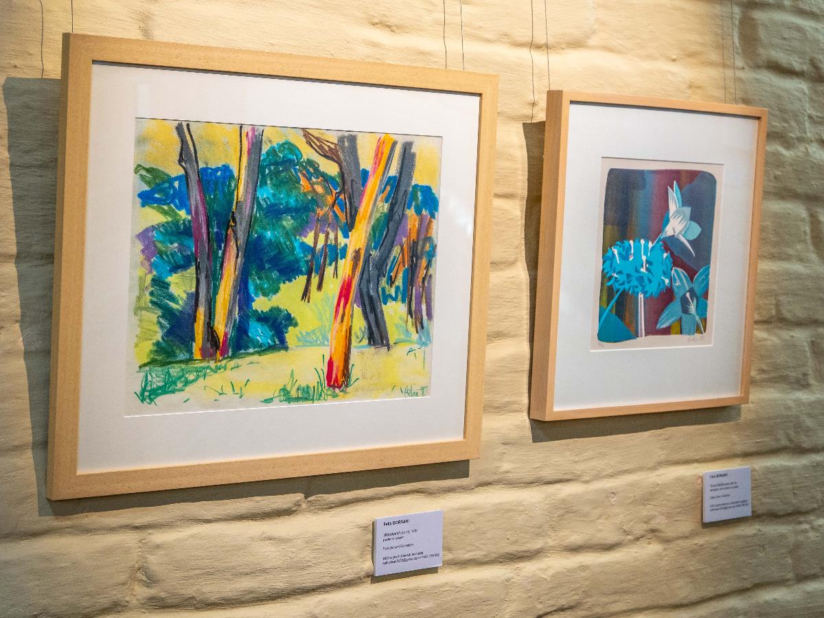 An image of two framed works. The left a drawing of colourful gum trees, the right a print of blue flowers