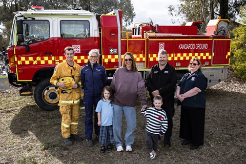 A group of adults and children standing in front of a large fire truck