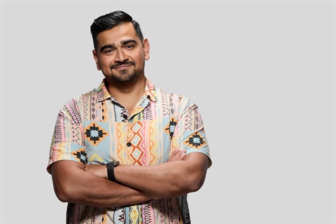 A man in a brightly coloured shirts smiles with his arms crossed