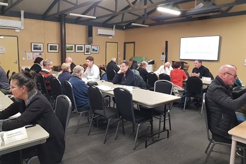 A group of adults are sitting at tables in a community hall